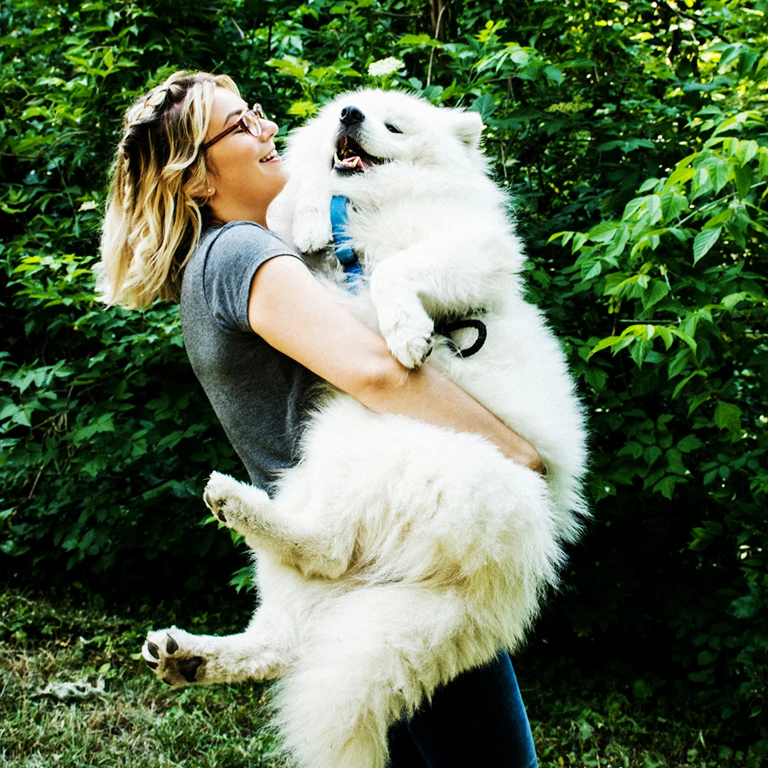 Woman hugging a large white dog in a green park.